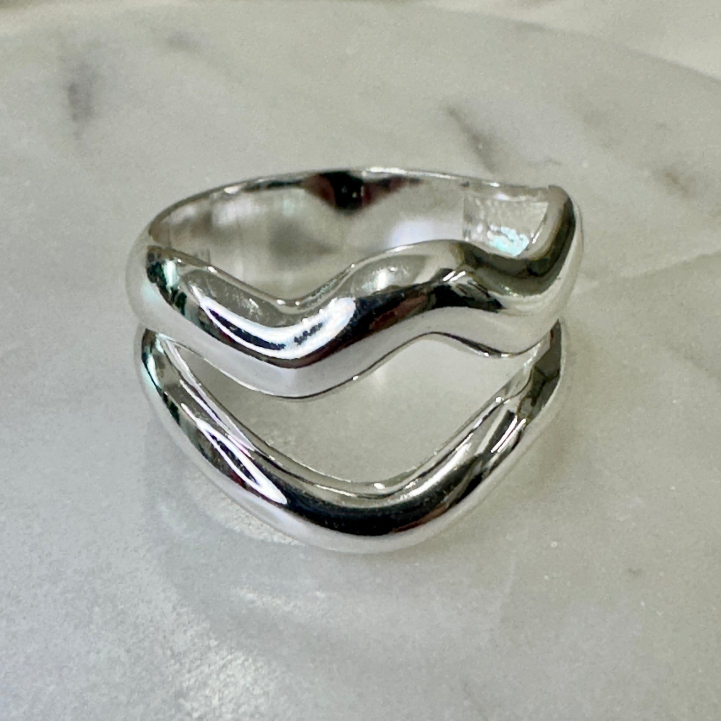 Silver ring with wavy design on a light gray background